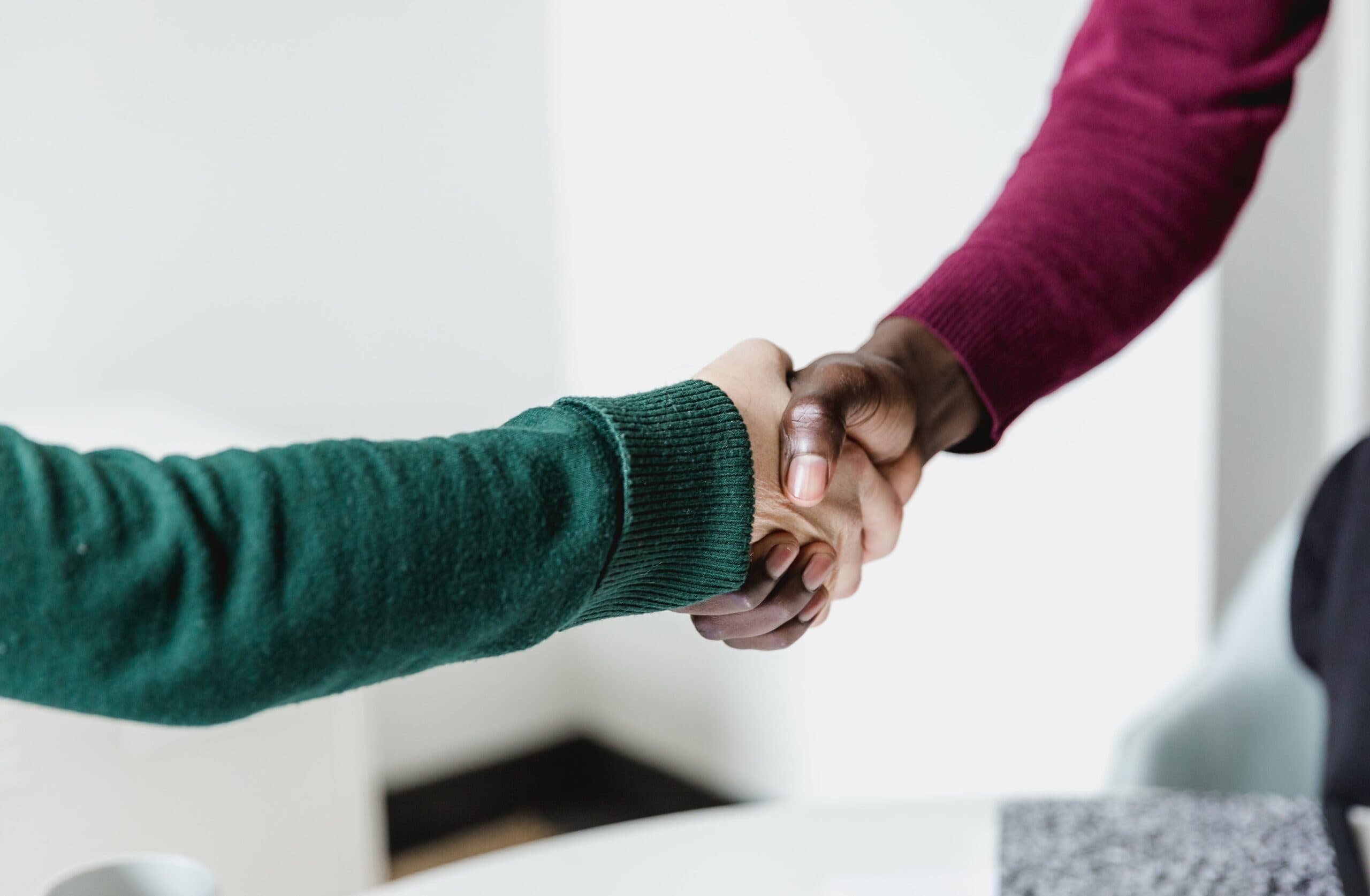 Two people shaking hands, one in a maroon jumper and one in a dark green jumper